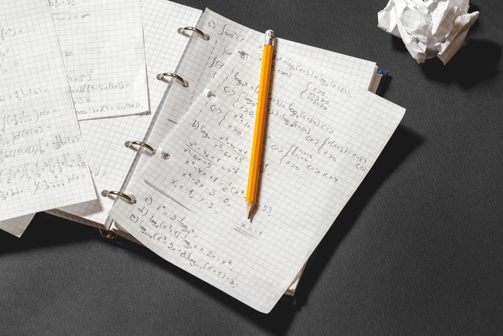 Solving a mathematical problem in a notebook. Crumpled piece of paper on black desk.