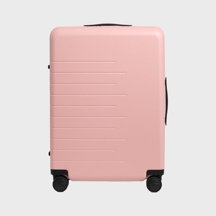 Pink suitcase stands on four wheels; it has horizontal grooves and black handles, set against a plain gray background.